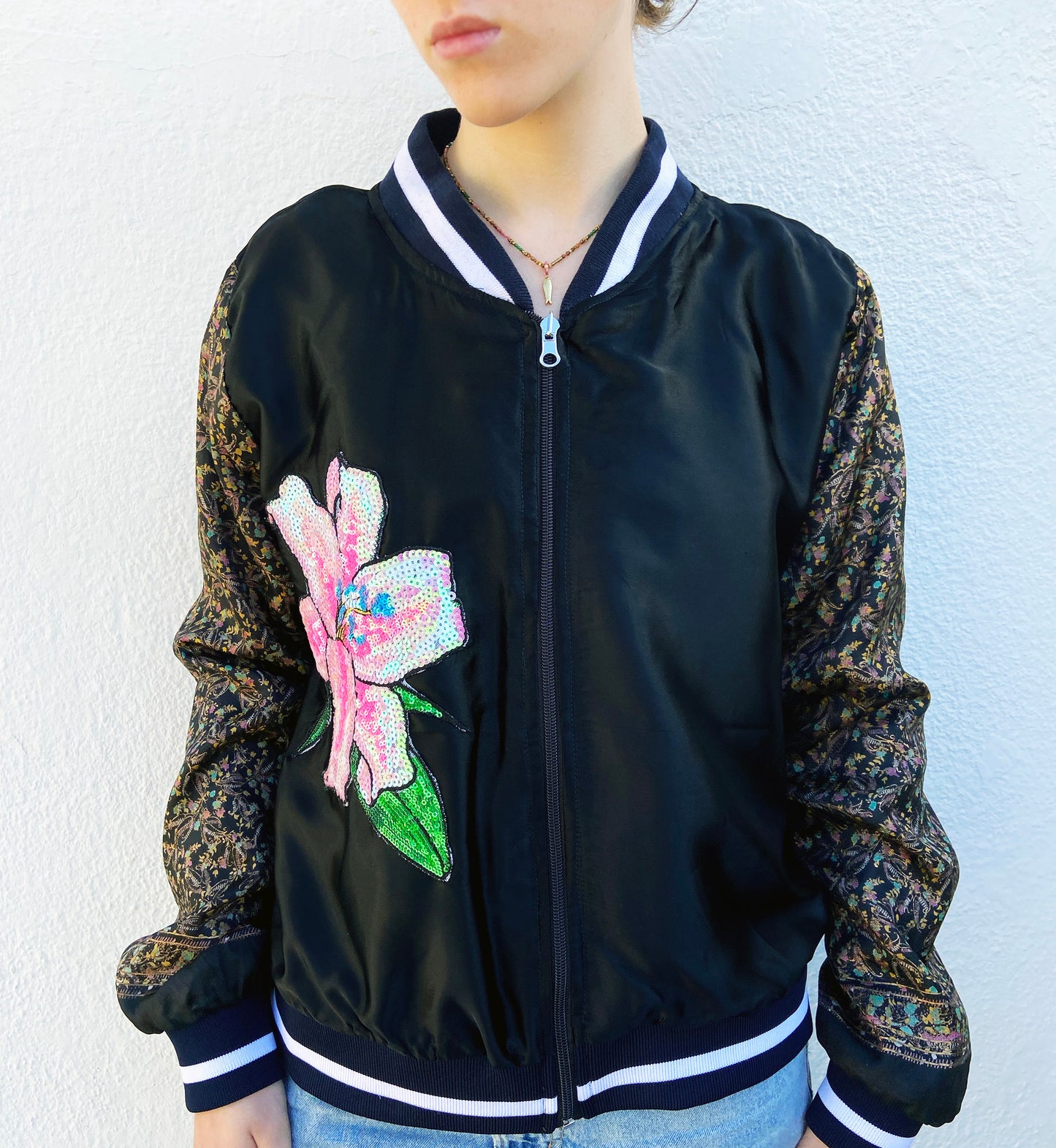 Black bomber jacket with floral sleeves and a pink flower design on a white background