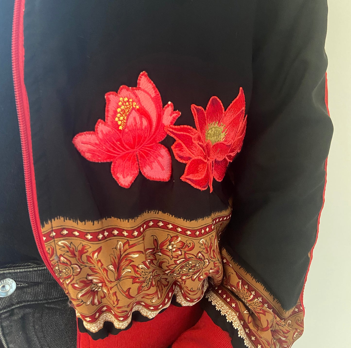 Traditional embroidered garment with red flowers and intricate patterns on a black background