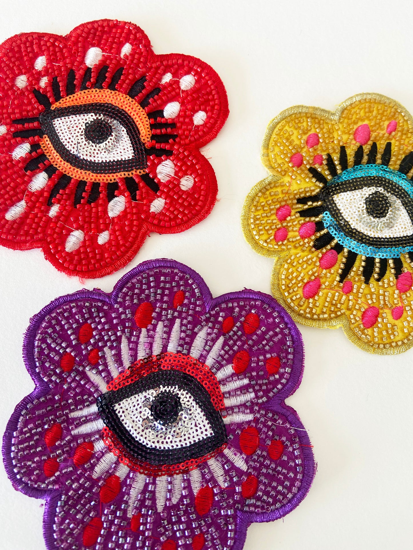 Three colorful embroidered patches with eye designs on a white background