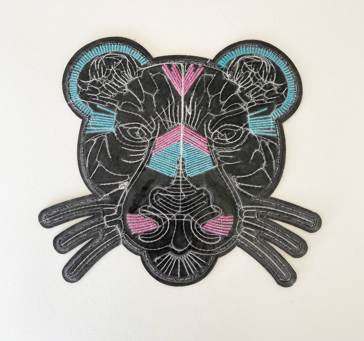 The back of an embroidered patch of a panther head with pink and blue accents on a white background