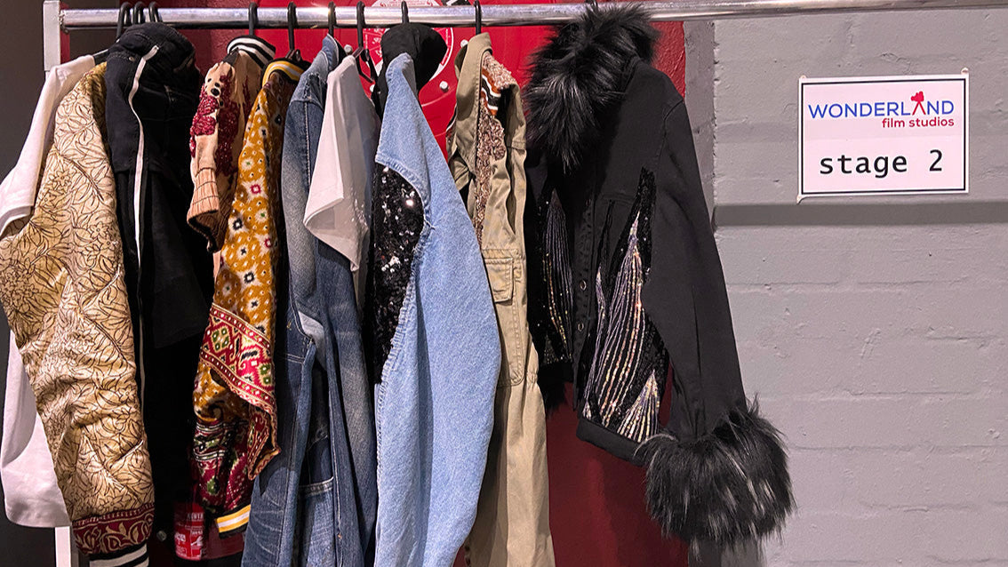 Clothing rack with various jackets against a red wall with a 'Wonderland' sign.