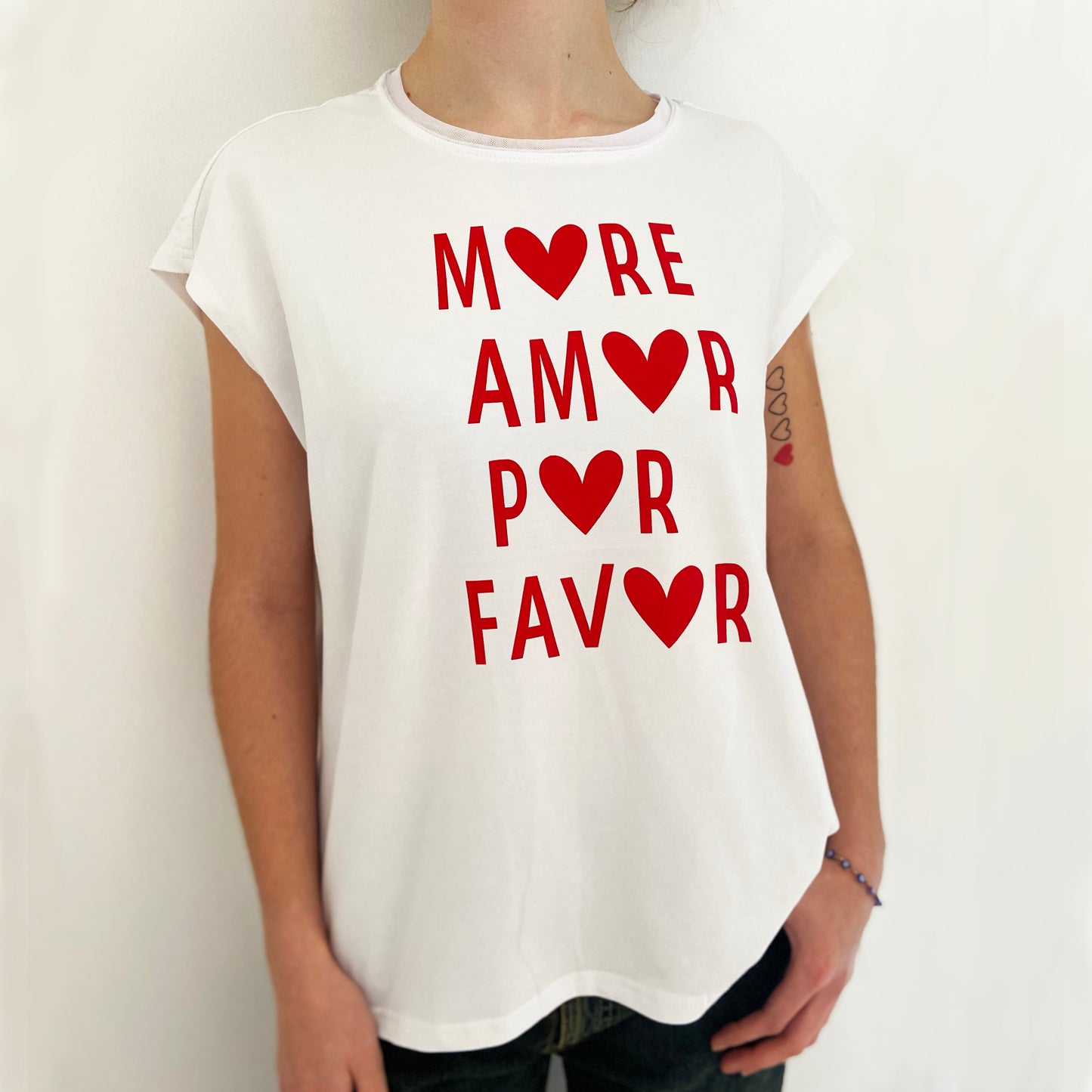 White t-shirt with red text and heart symbols worn by a person on a plain background