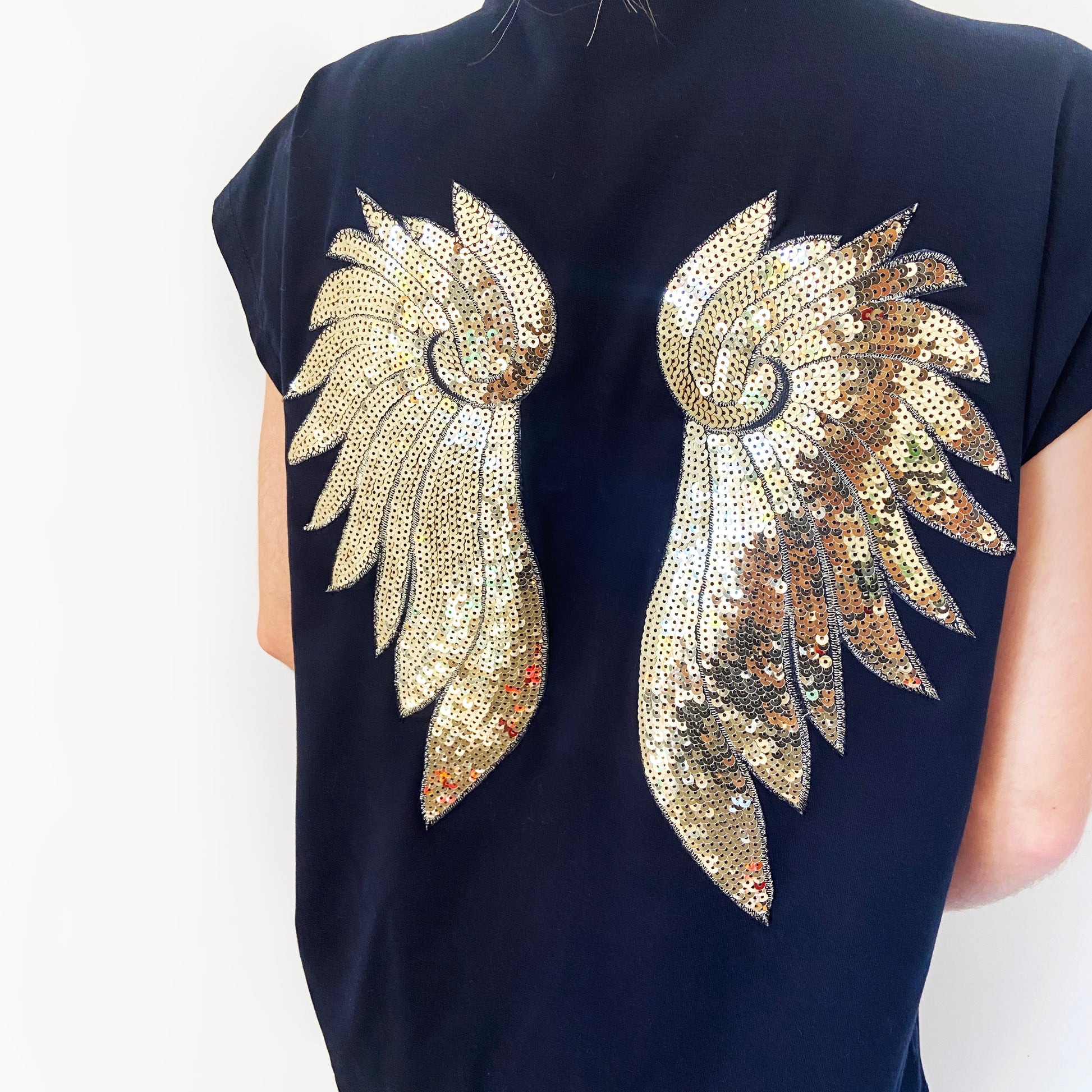 Black top with gold sequin angel wings motif on a plain background