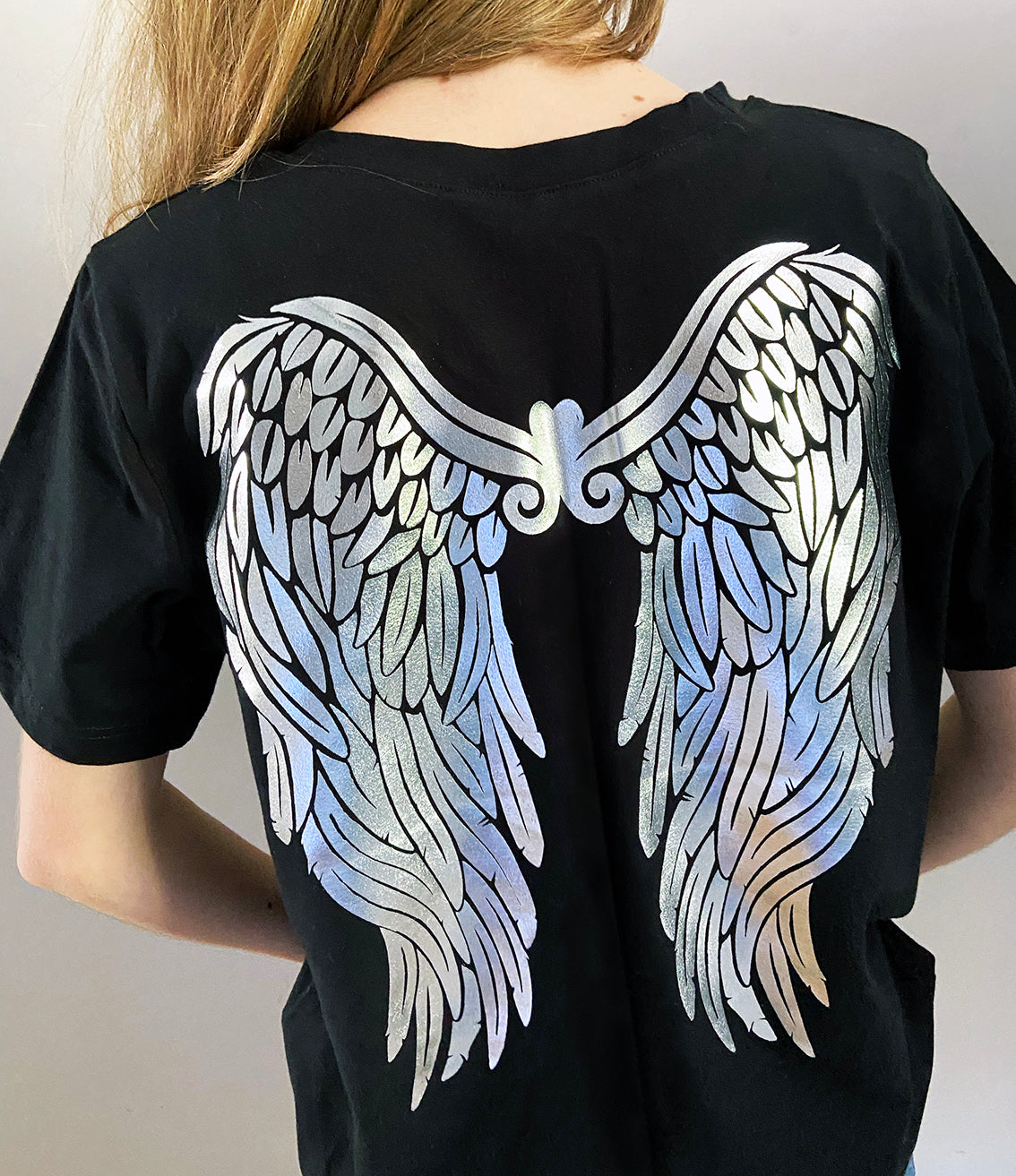 back of young girl wearing a black t-shirt with silver angel wings