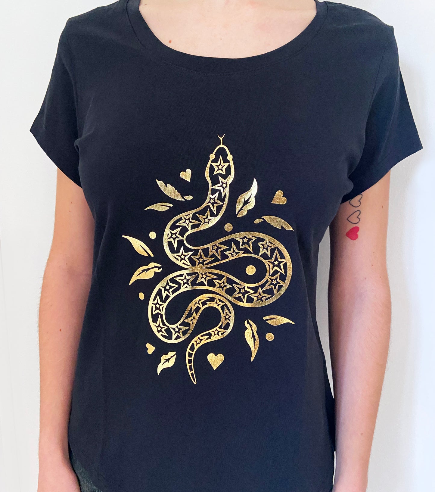 Black t-shirt with gold snake design worn by a person on a white background