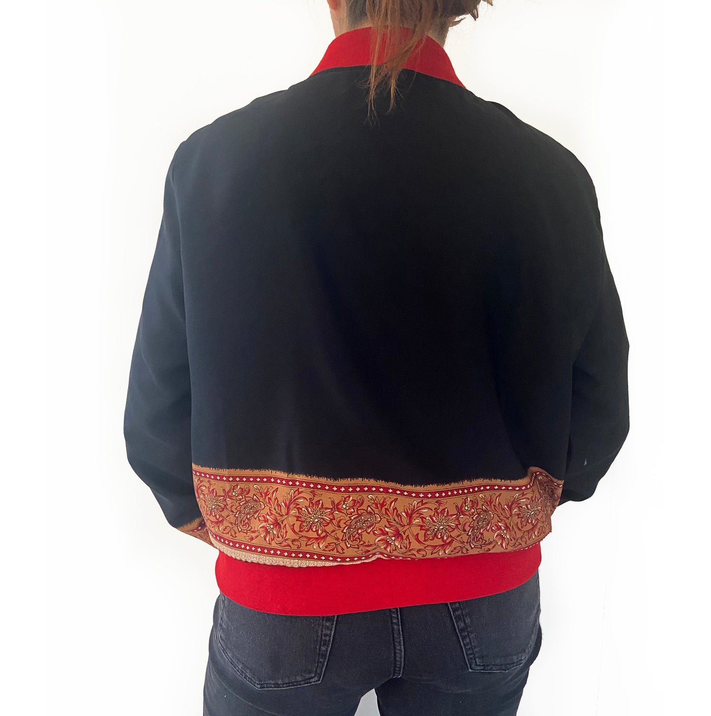 Person wearing a black jacket with a red inner lining and decorative back panel on a white background