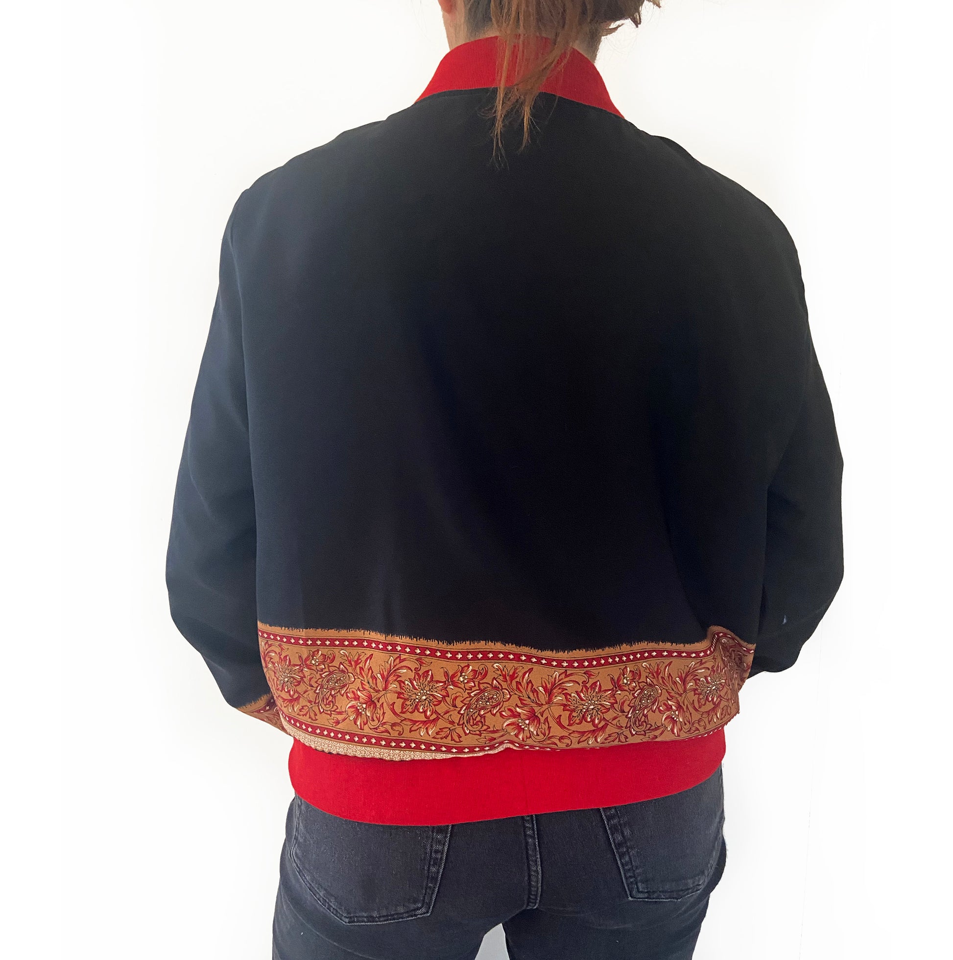 Person wearing a black jacket with a red inner lining and decorative back panel on a white background