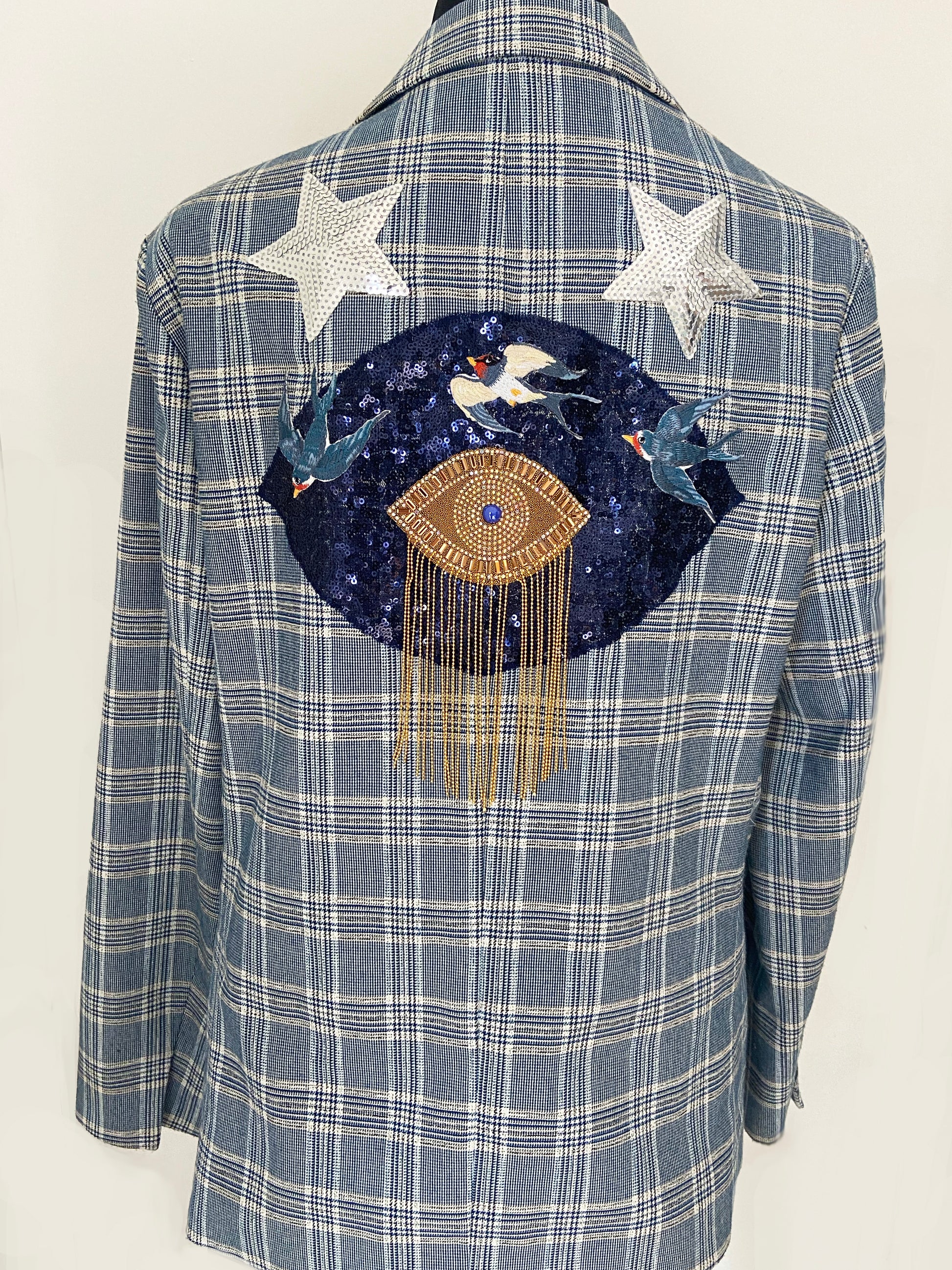 Blue plaid shirt with a decorative patch featuring birds and an eye symbol on a white background