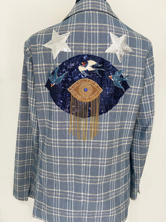 Blue plaid shirt with a decorative patch featuring birds and an eye symbol on a white background