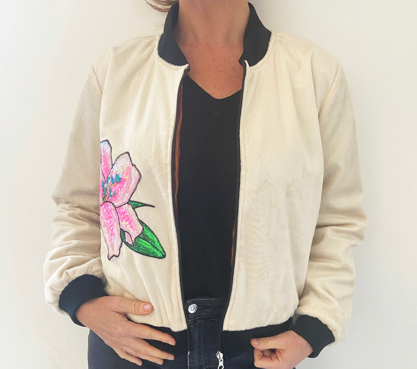 Person wearing a cream jacket with a floral design on a plain background
