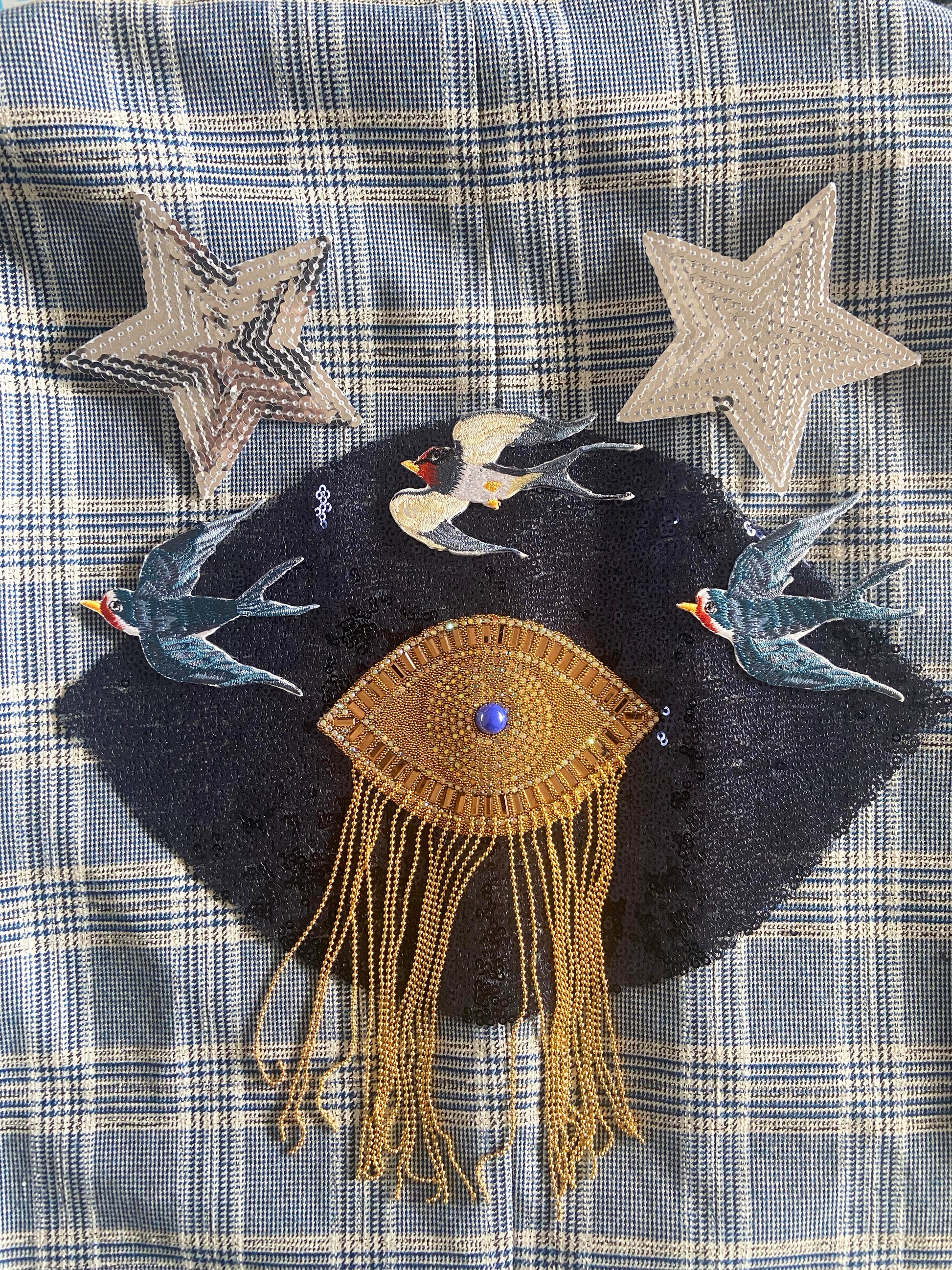 Embroidered patch with birds and an eye design on a plaid fabric background