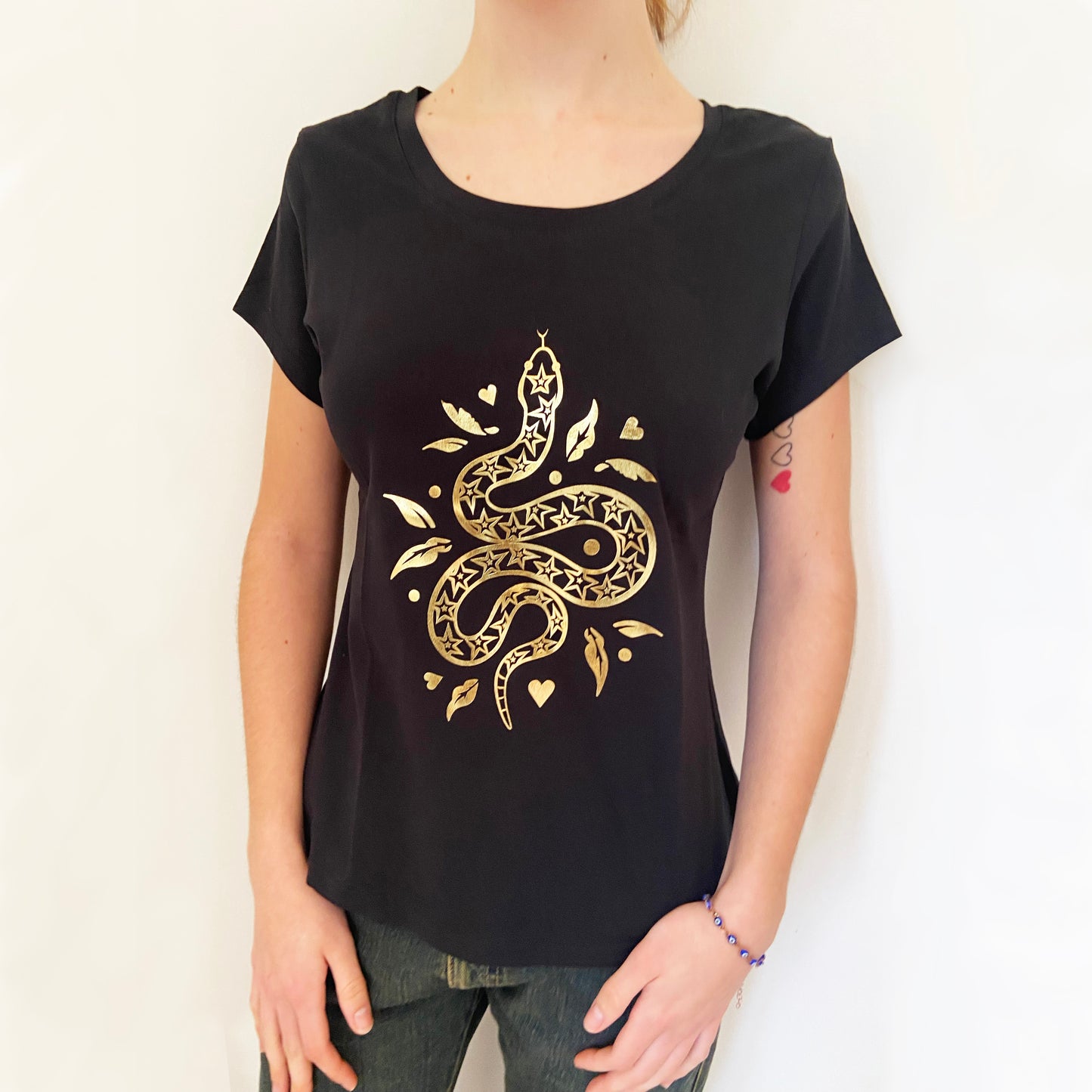 Black t-shirt with gold snake design worn by a person on a white background