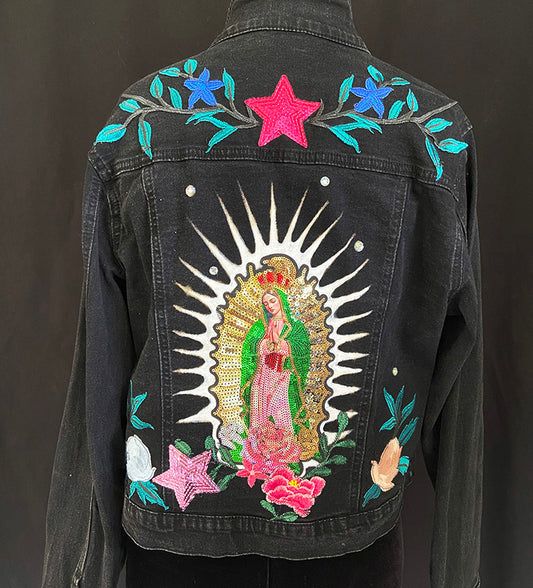 Black denim jacket with embroidered designs on the back, including a star, flowers, and a central figure.