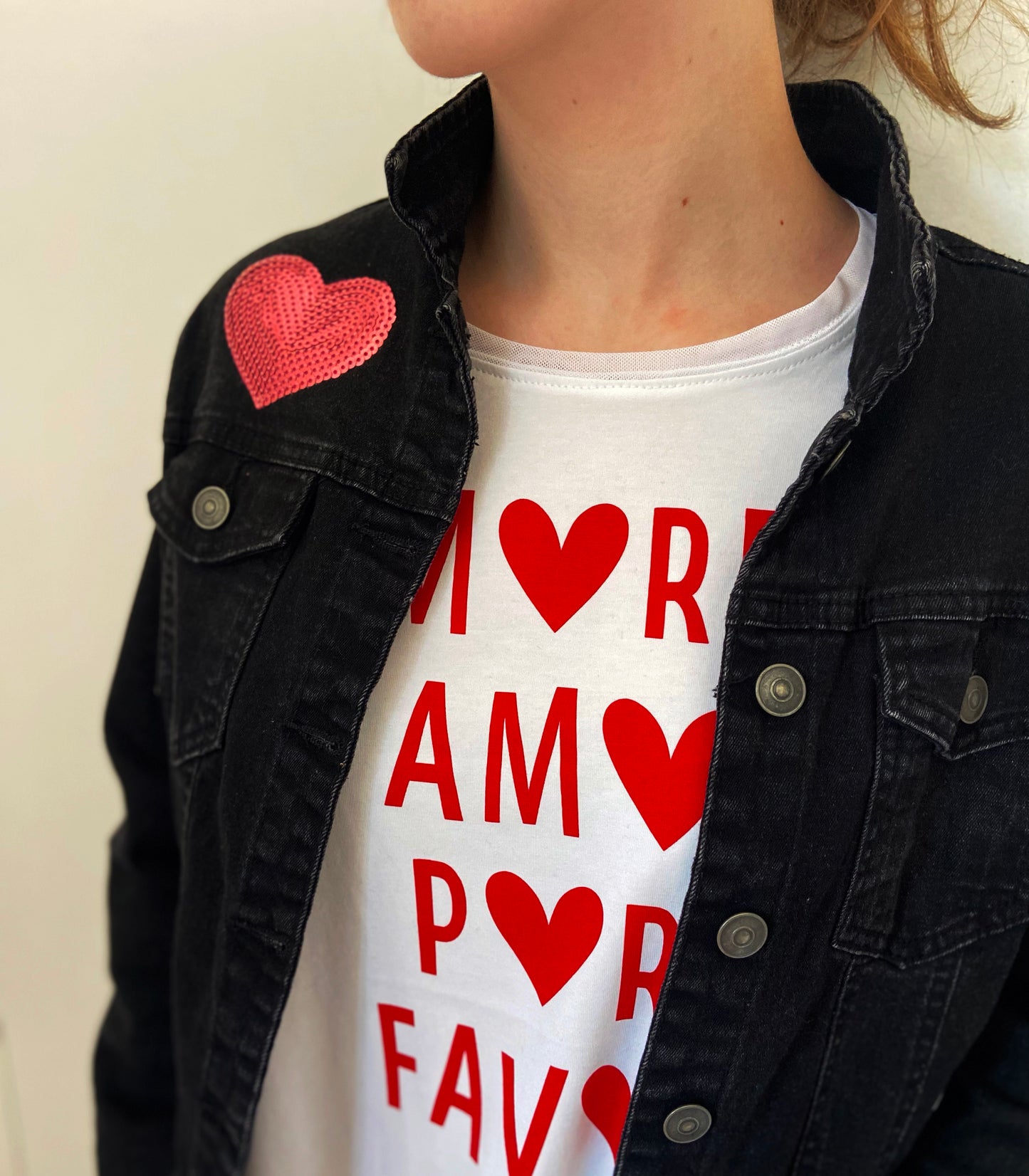 Person wearing a black jacket with a heart patch and a white t-shirt with red text and hearts.