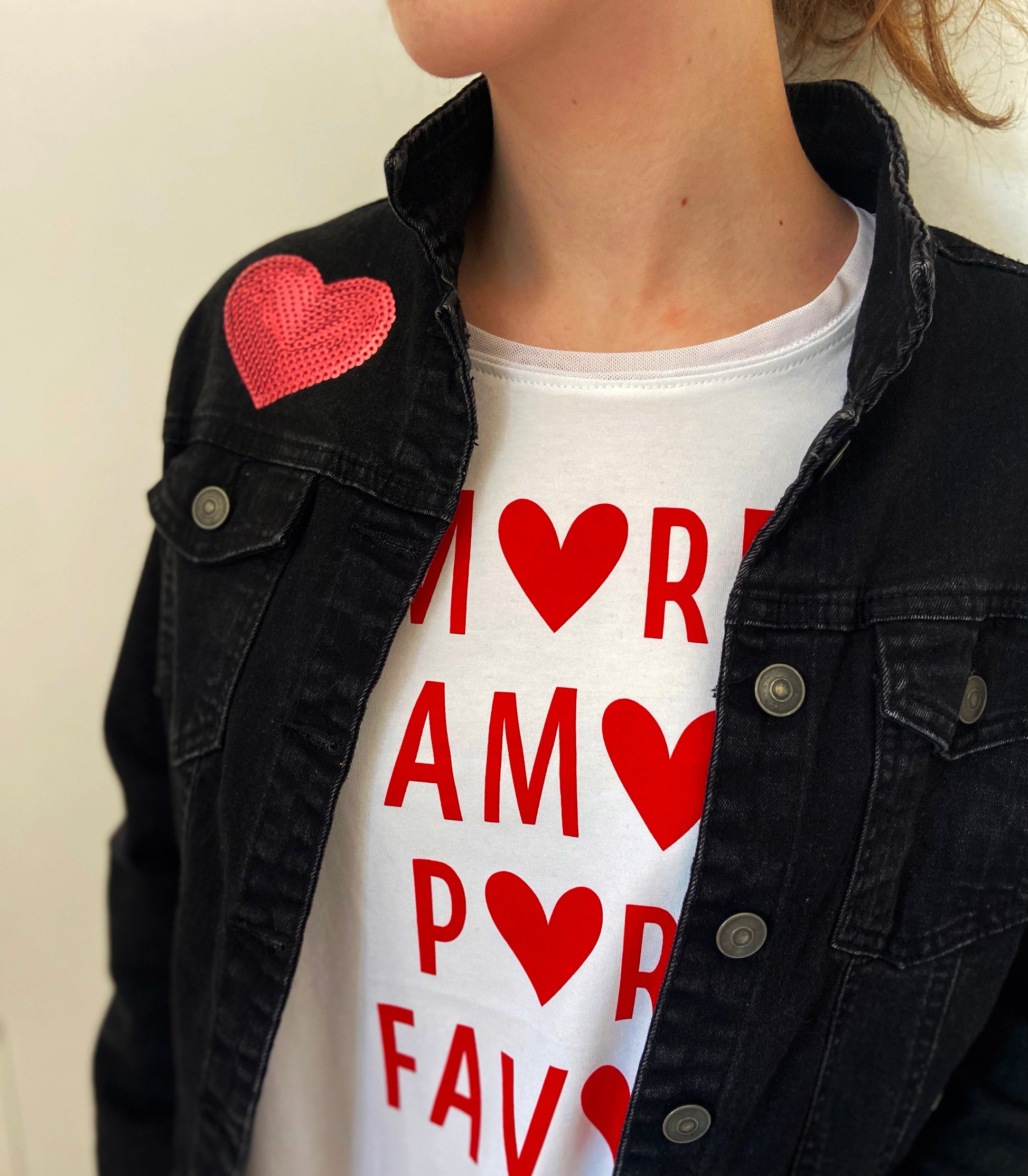 Person wearing a black jacket with a heart patch and a white t-shirt with red text and hearts.
