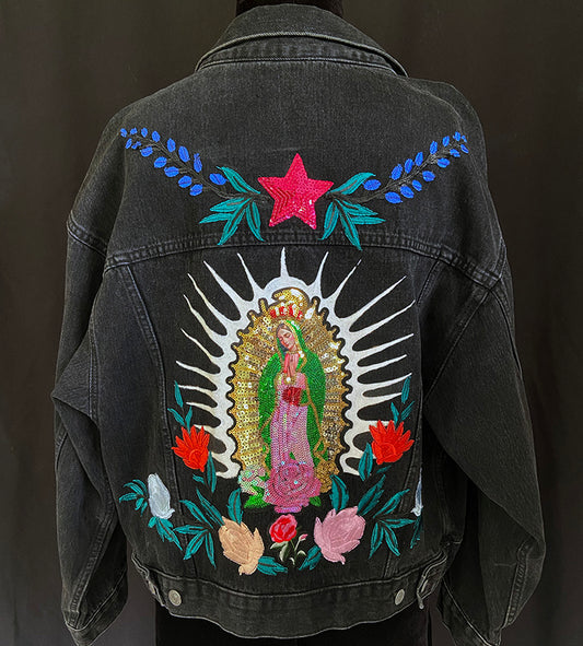 Black denim jacket with embroidered design of a religious figure and flowers on a dark background