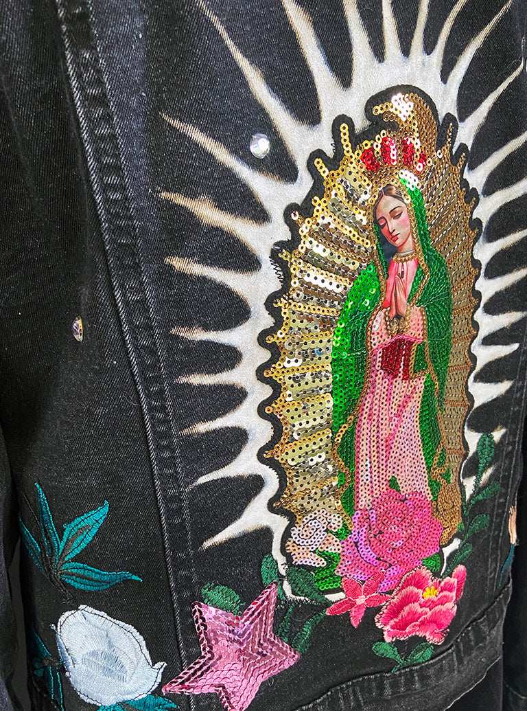 Embroidered design of a religious figure on a black denim jacket with floral and star details.