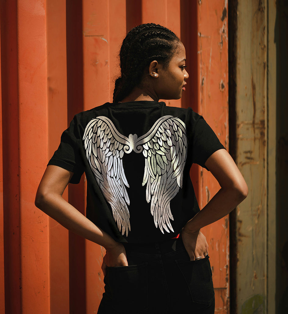 A person wearing a black t-shirt with silver foil printed angel wings on the back, standing in front of a red container.
