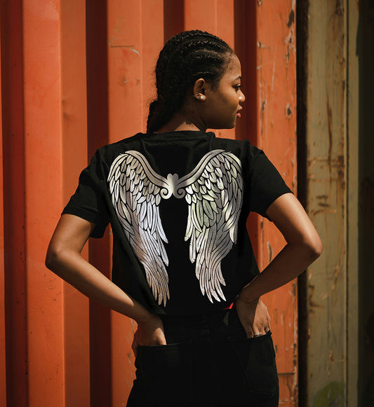 A person wearing a black t-shirt with silver foil printed angel wings on the back, standing in front of a red container.