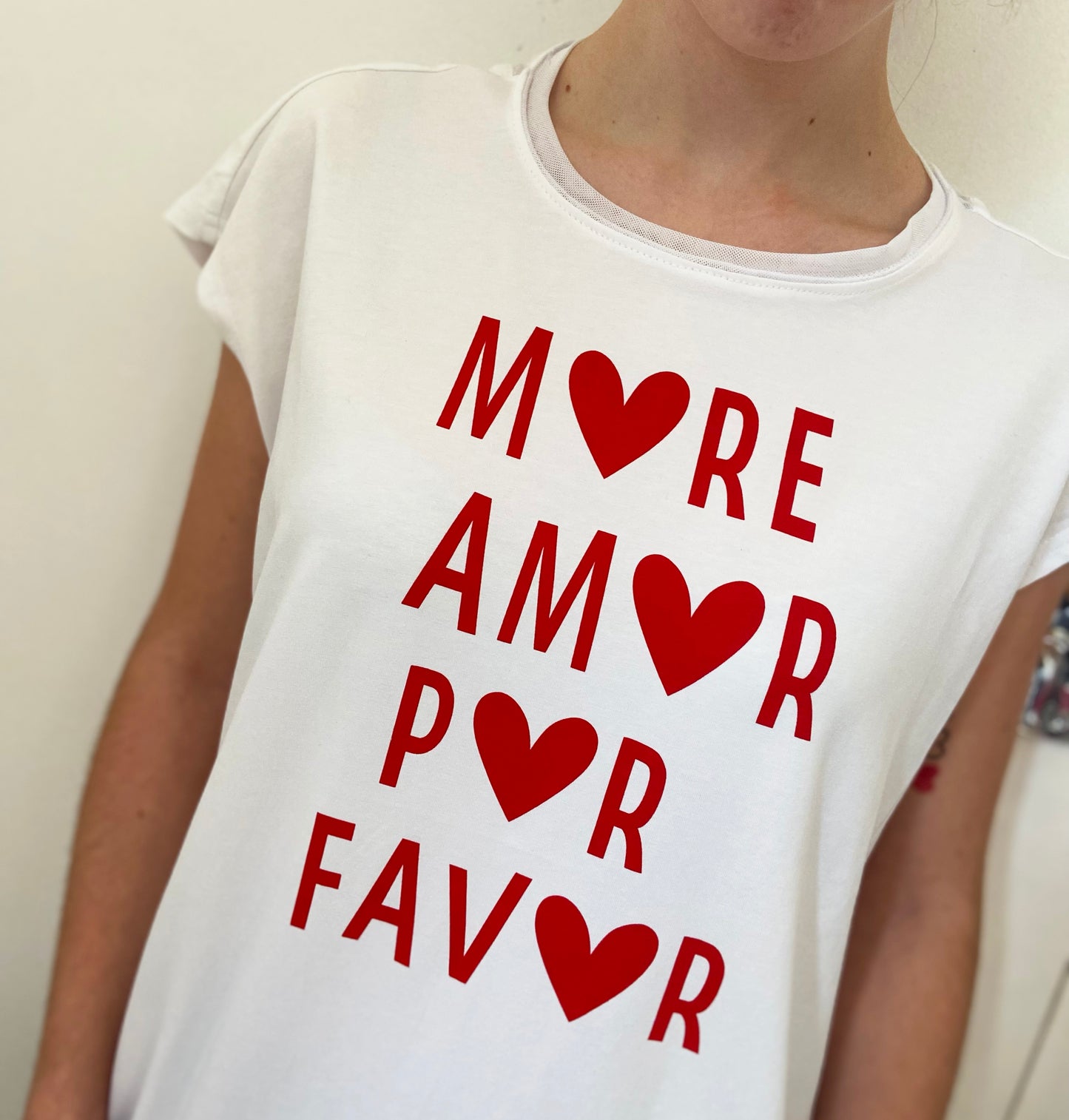 White t-shirt with red text and heart symbols worn by a person against a plain background