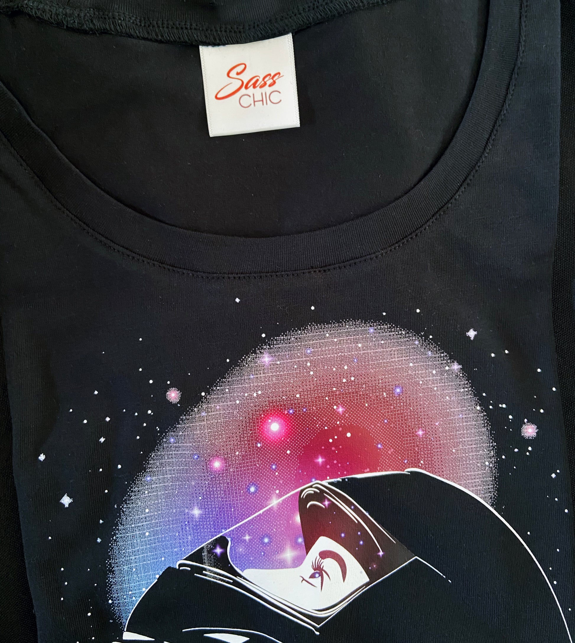 Black t-shirt with a graphic design of a character in a space helmet against a starry background, featuring the brand 'Sass Chic'.