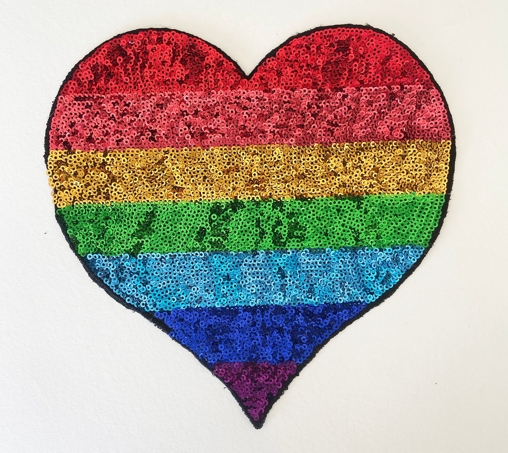 Heart-shaped patch with rainbow sequin pattern on a white background