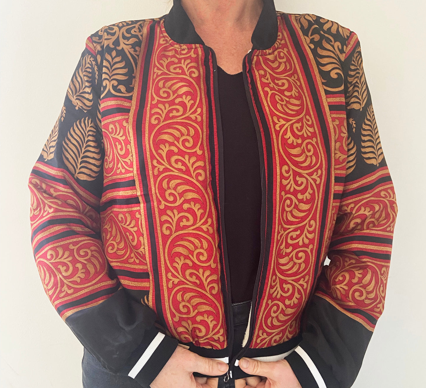 Person wearing a patterned jacket with red, black, and gold design on a plain background