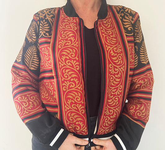 Person wearing a patterned jacket with red, black, and gold design on a plain background