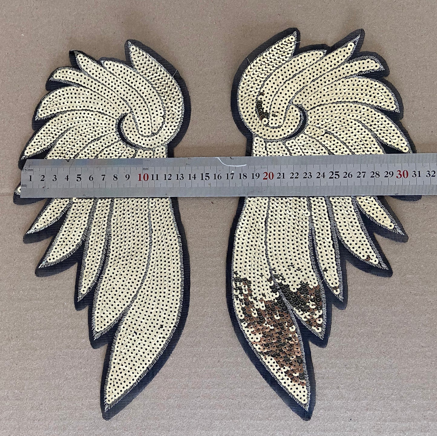 Sequinned wing-shaped patches with a ruler for scale on a brown background