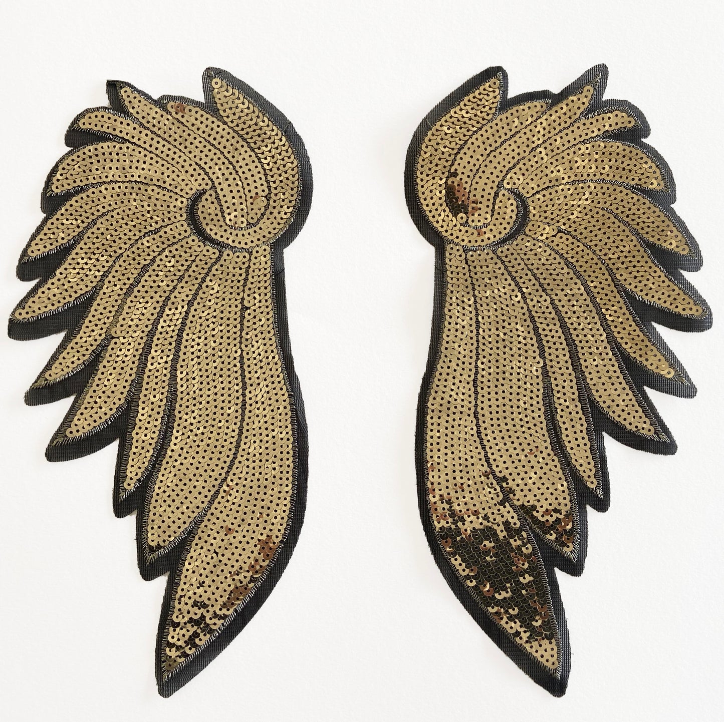 Pair of gold and black wing-shaped  sequin patches on a white background