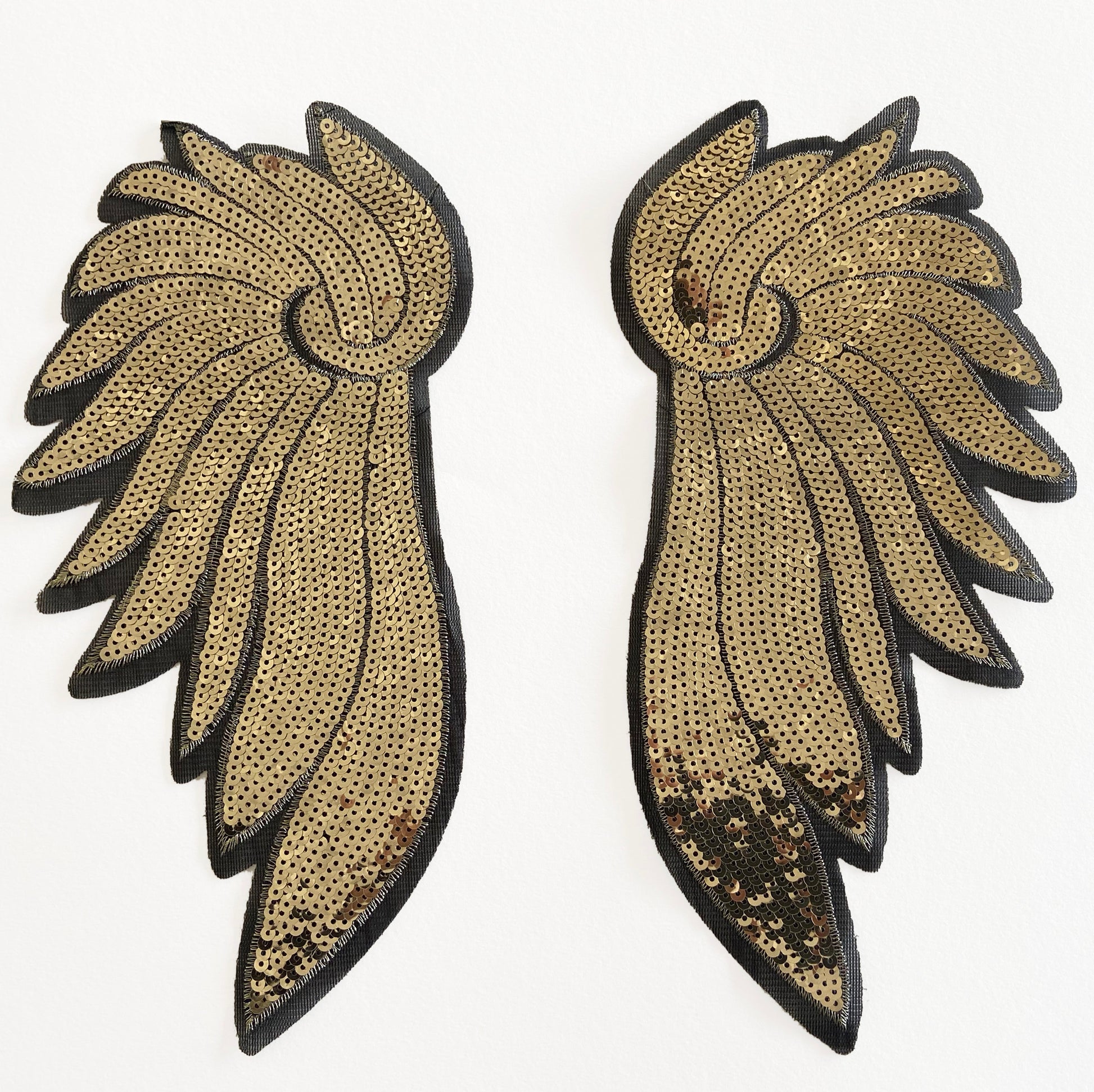Pair of gold and black wing-shaped  sequin patches on a white background