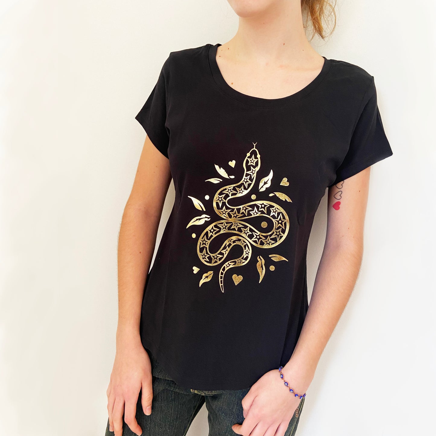 Person wearing a black t-shirt with a gold snake design on a plain background