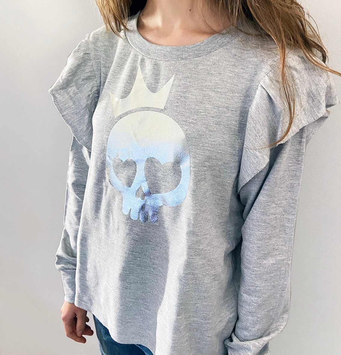 a person wearing a light grey shirt with silver foil skull print.