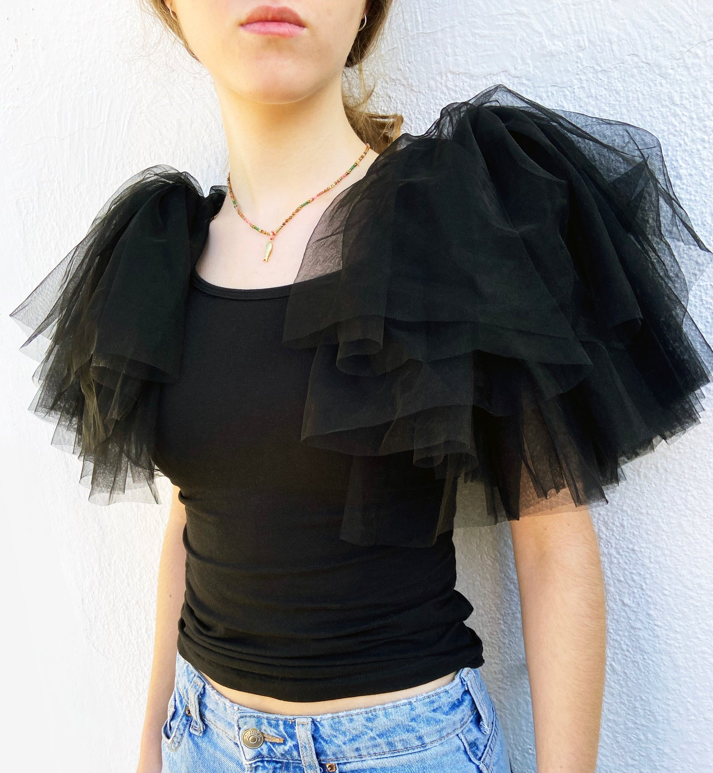 Person wearing a black top with ruffled tulle sleeves against a white background