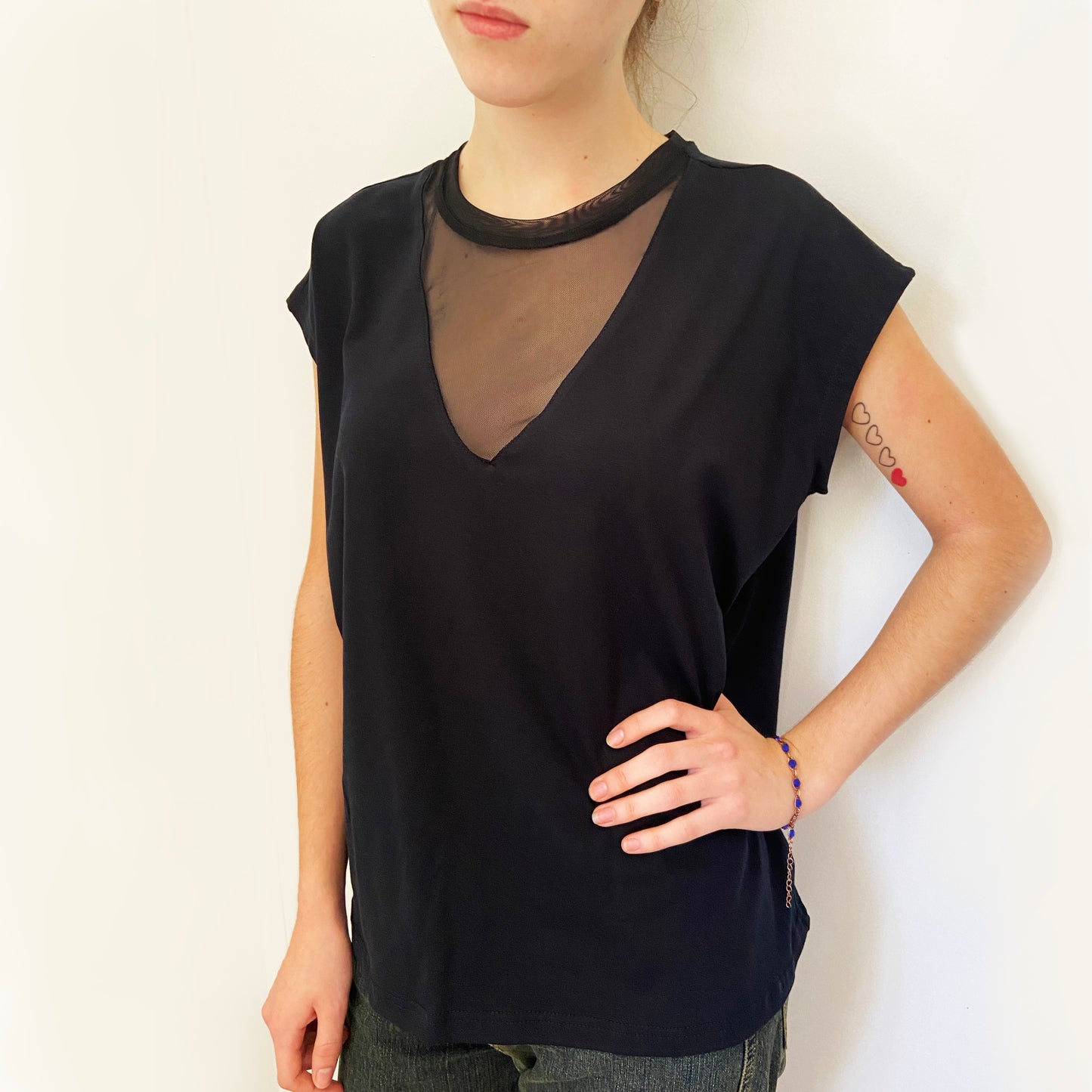 Person wearing a black sleeveless top with sheer neckline against a plain background