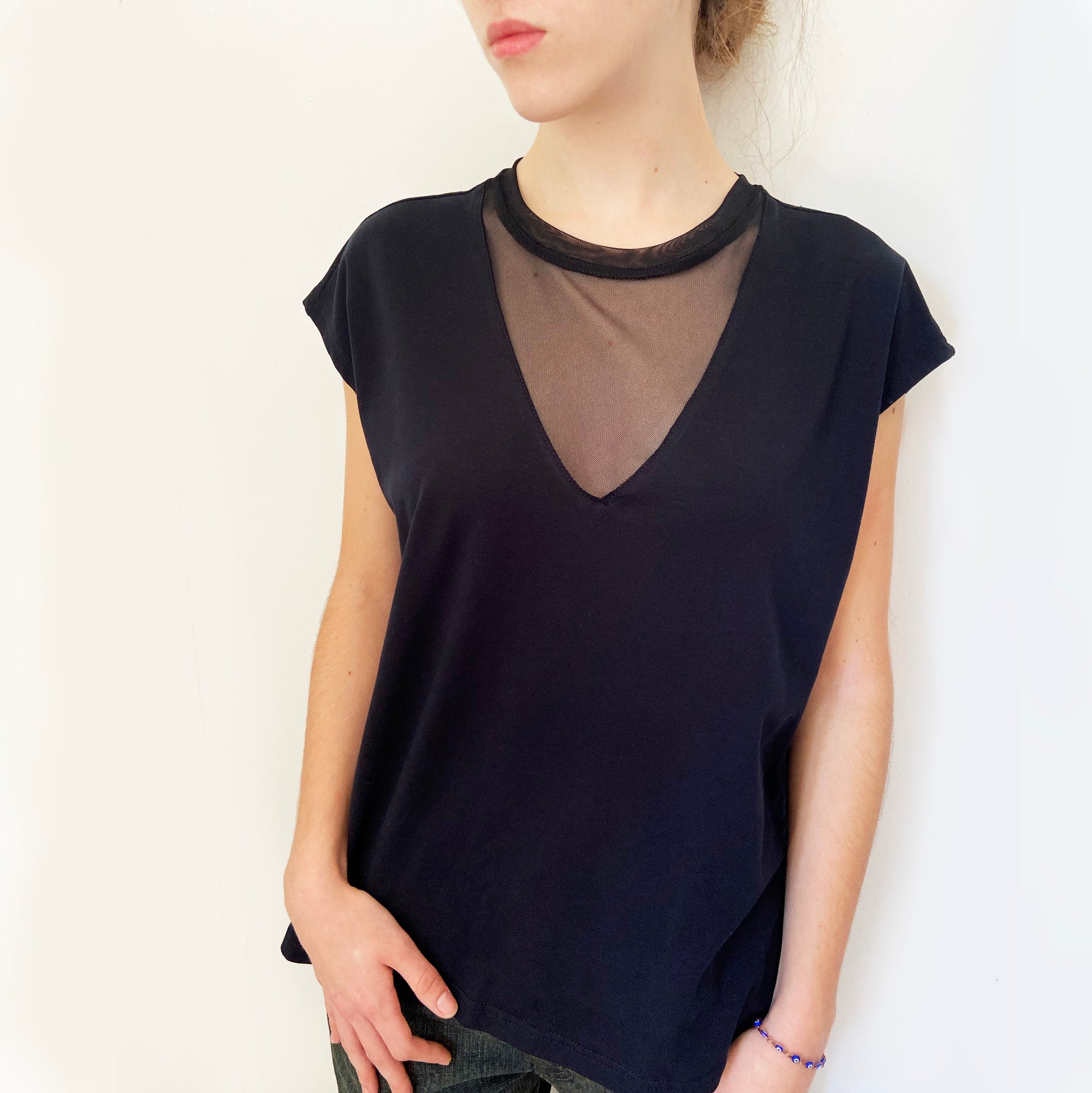Person wearing a black sleeveless top with sheer mesh detail on a white background