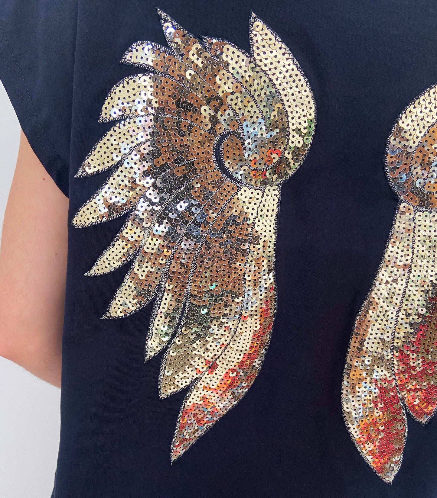 Black garment with gold sequin angel wings design on a plain background