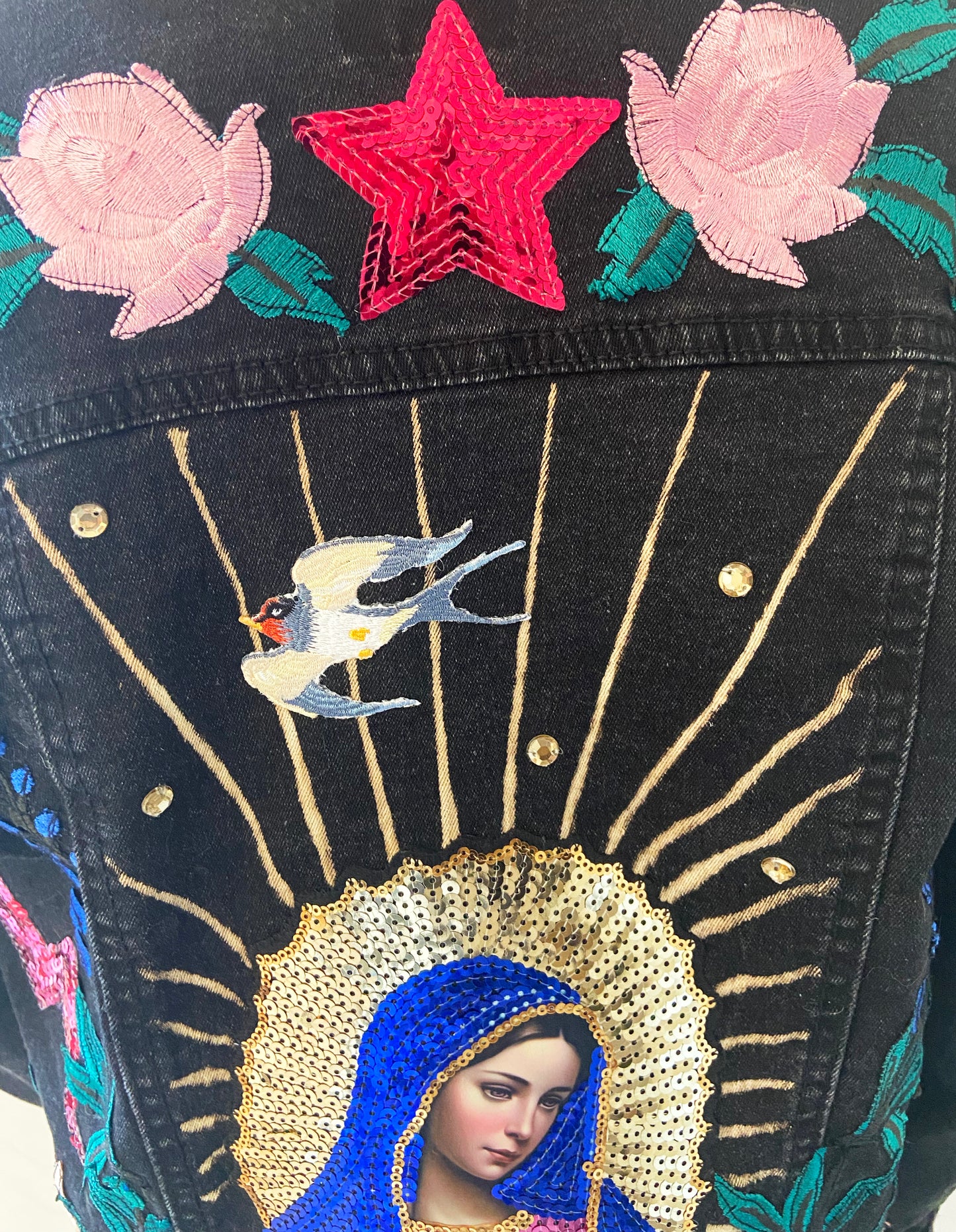 Embroidered design on a black background with a star, flowers, and a beaded depiction of a religious figure.