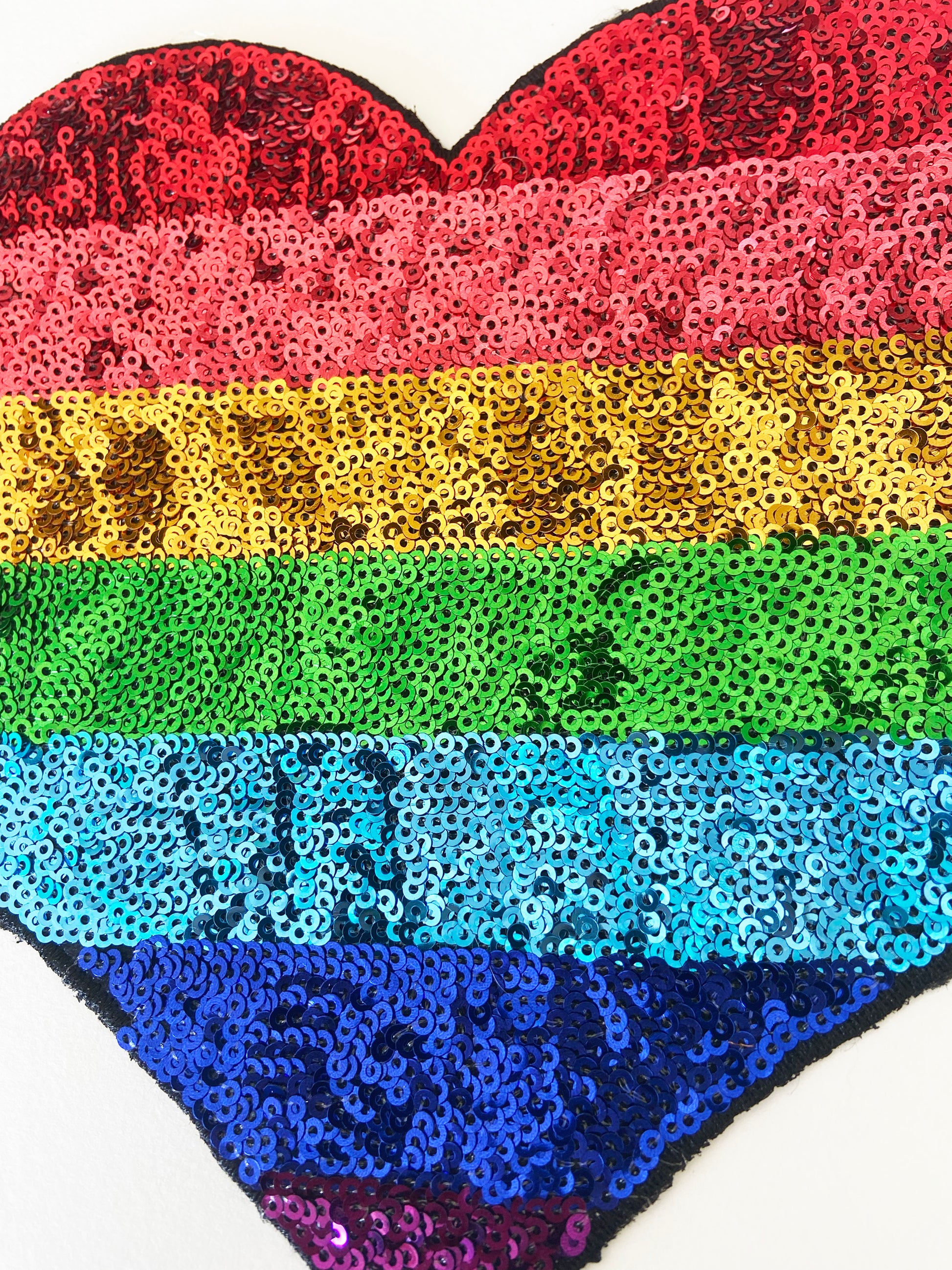 Heart-shaped object with rainbow sequin pattern on a white background