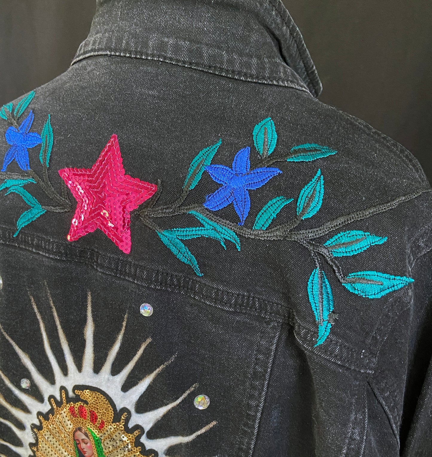 Black denim jacket with colorful star and floral embroidery on a dark background
