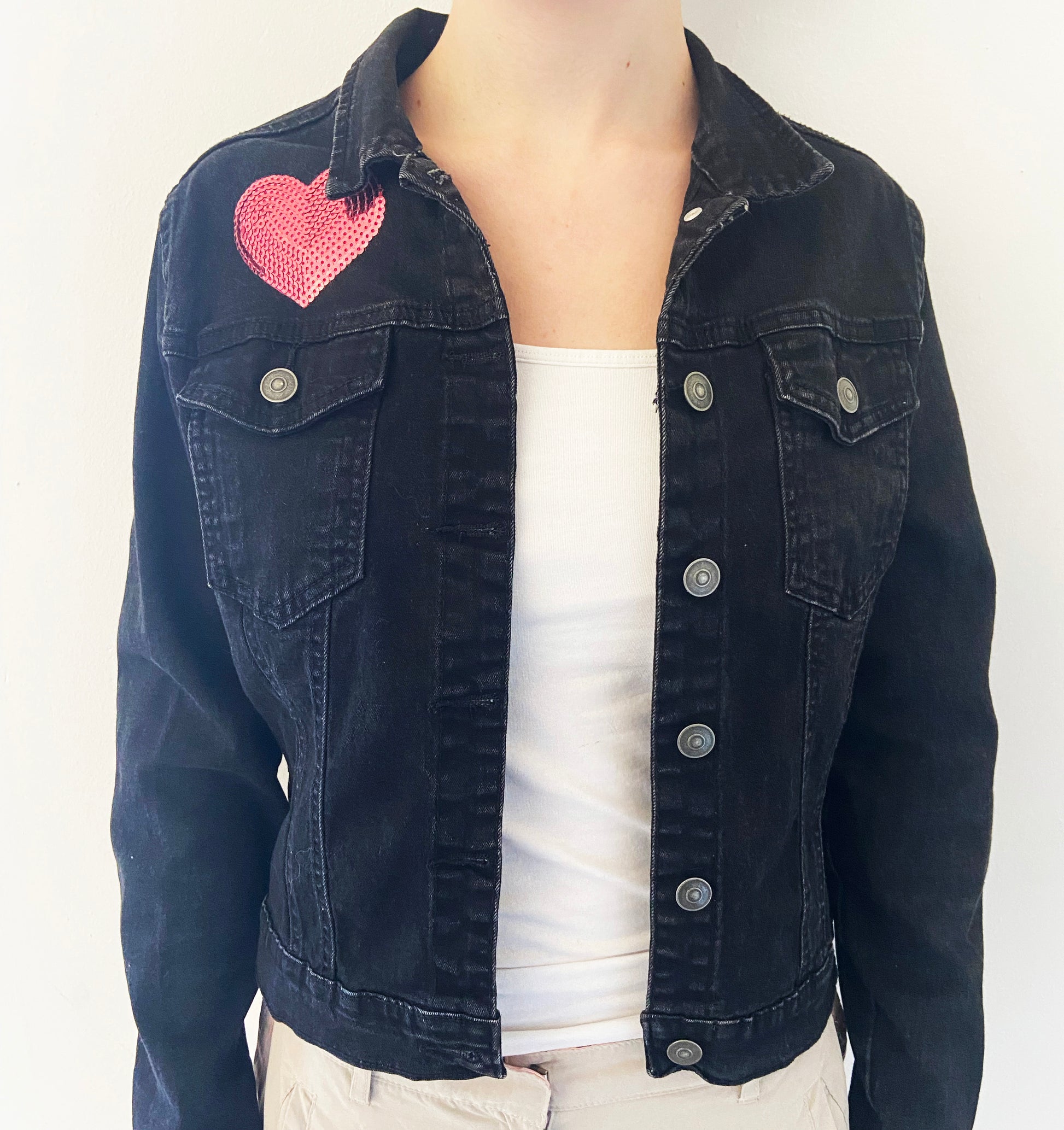 Black denim jacket with a pink heart patch on a white background