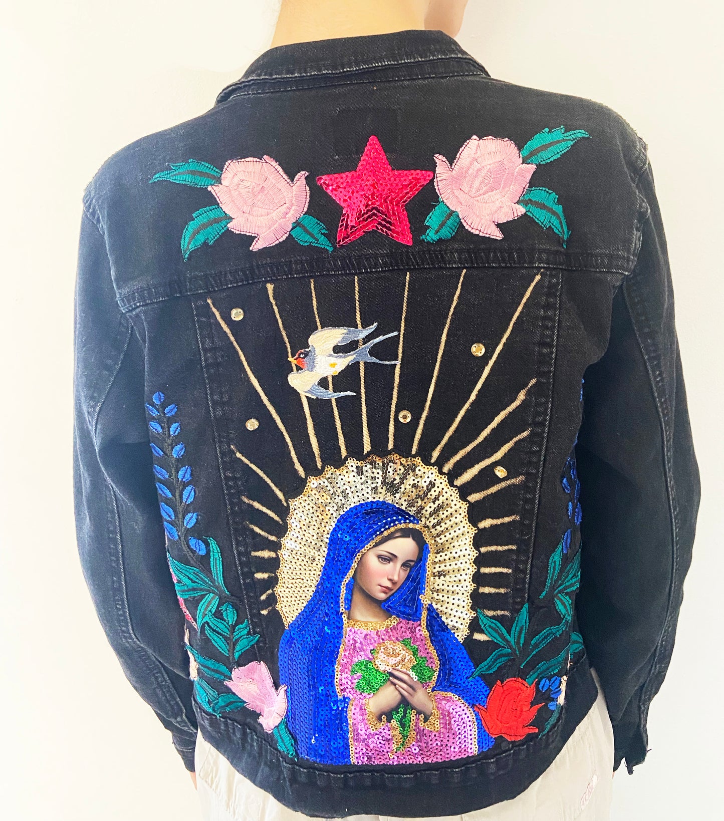 Black denim jacket with embroidered design of a religious figure, flowers, and a star.