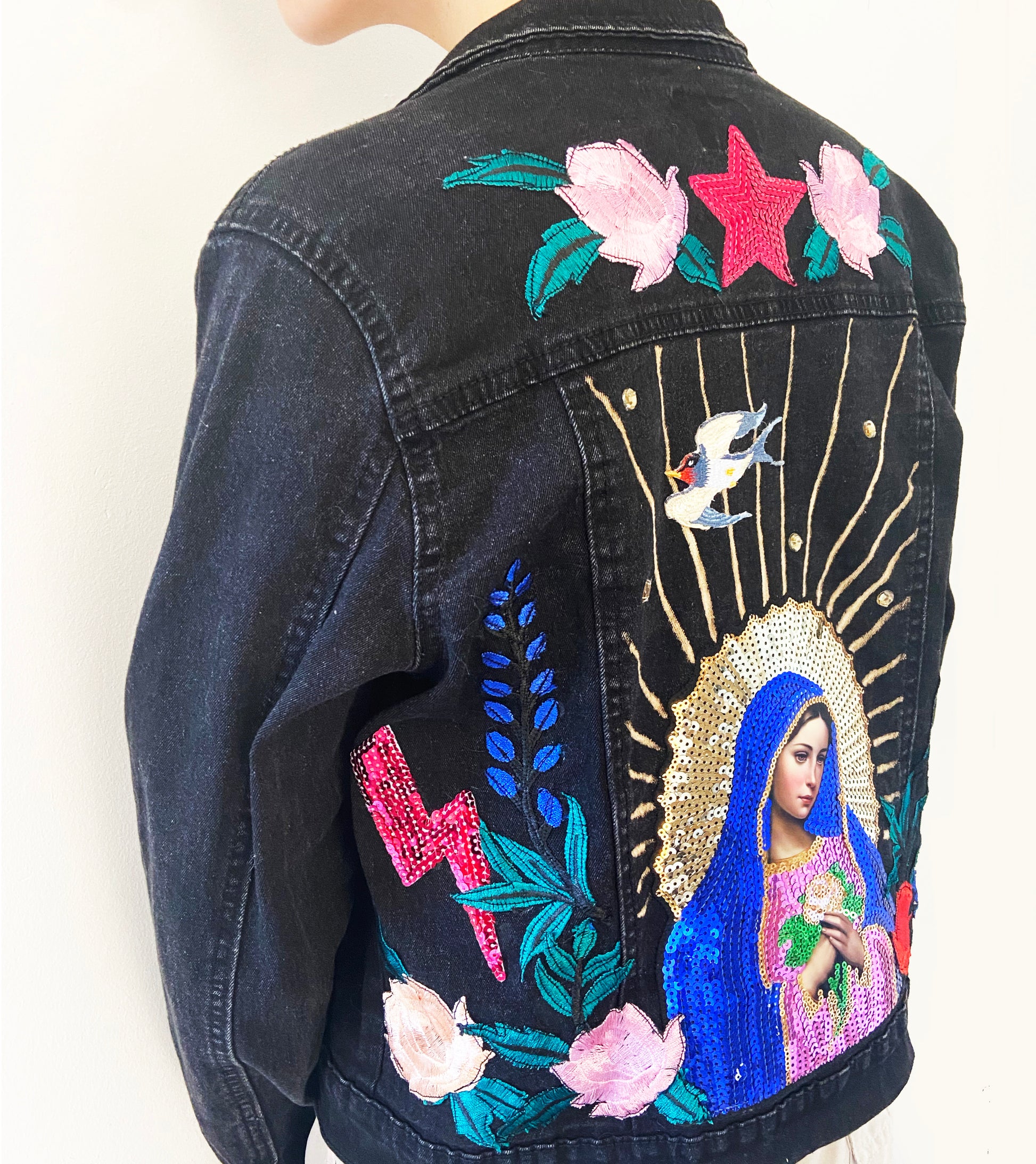 Black denim jacket with colorful embroidery and designs on a white background