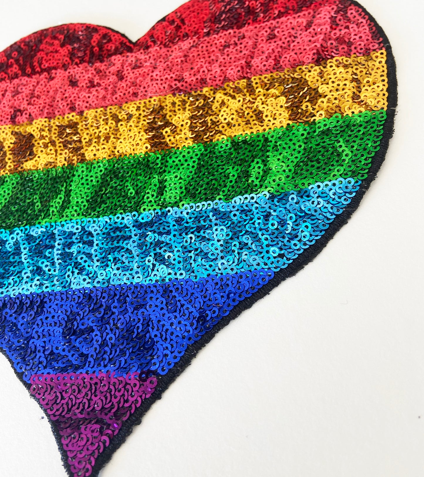 Heart-shaped patch with rainbow sequin pattern on a white background