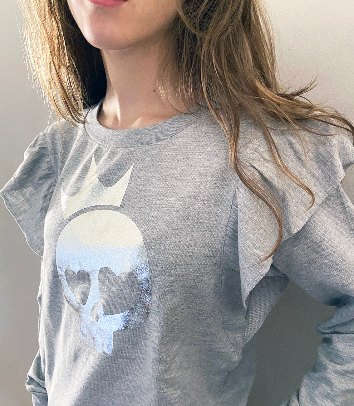 A close up of a person wearing a light grey shirt with silver foil skull print.