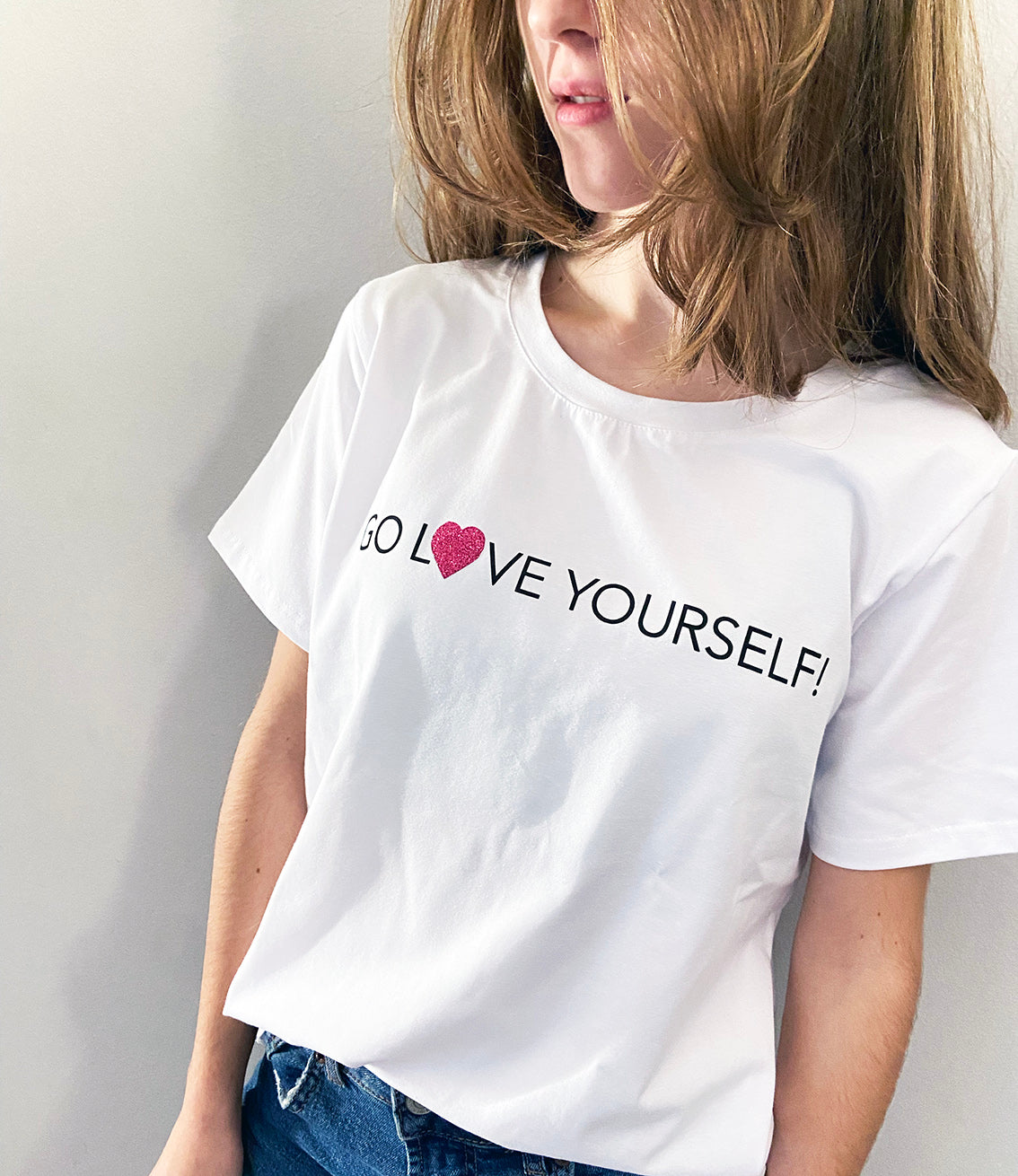 A person wearing a white t-shirt with the text 'GO LOVE YOURSELF!' and a glitter vinyl heart graphic on the front.