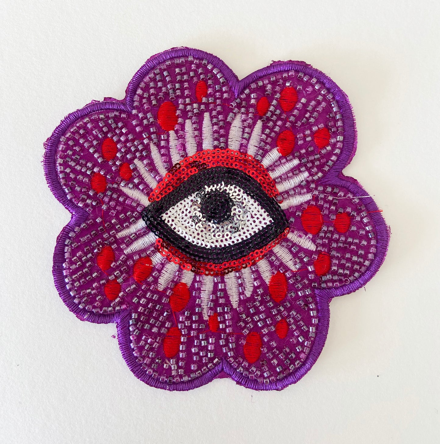 Embroidered patch with a purple flower design and central eye on a white background