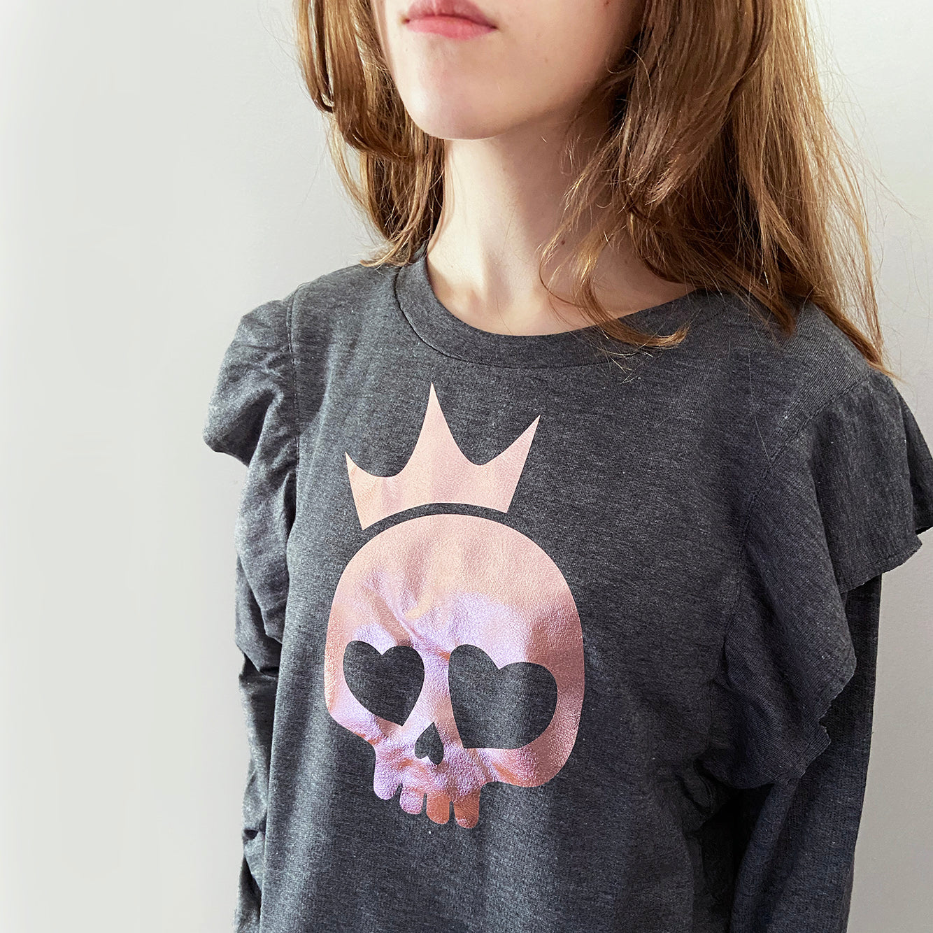 A person wearing a charcoal grey sweatshirt with a rose gold foil print of a skull with a crown design on the front.