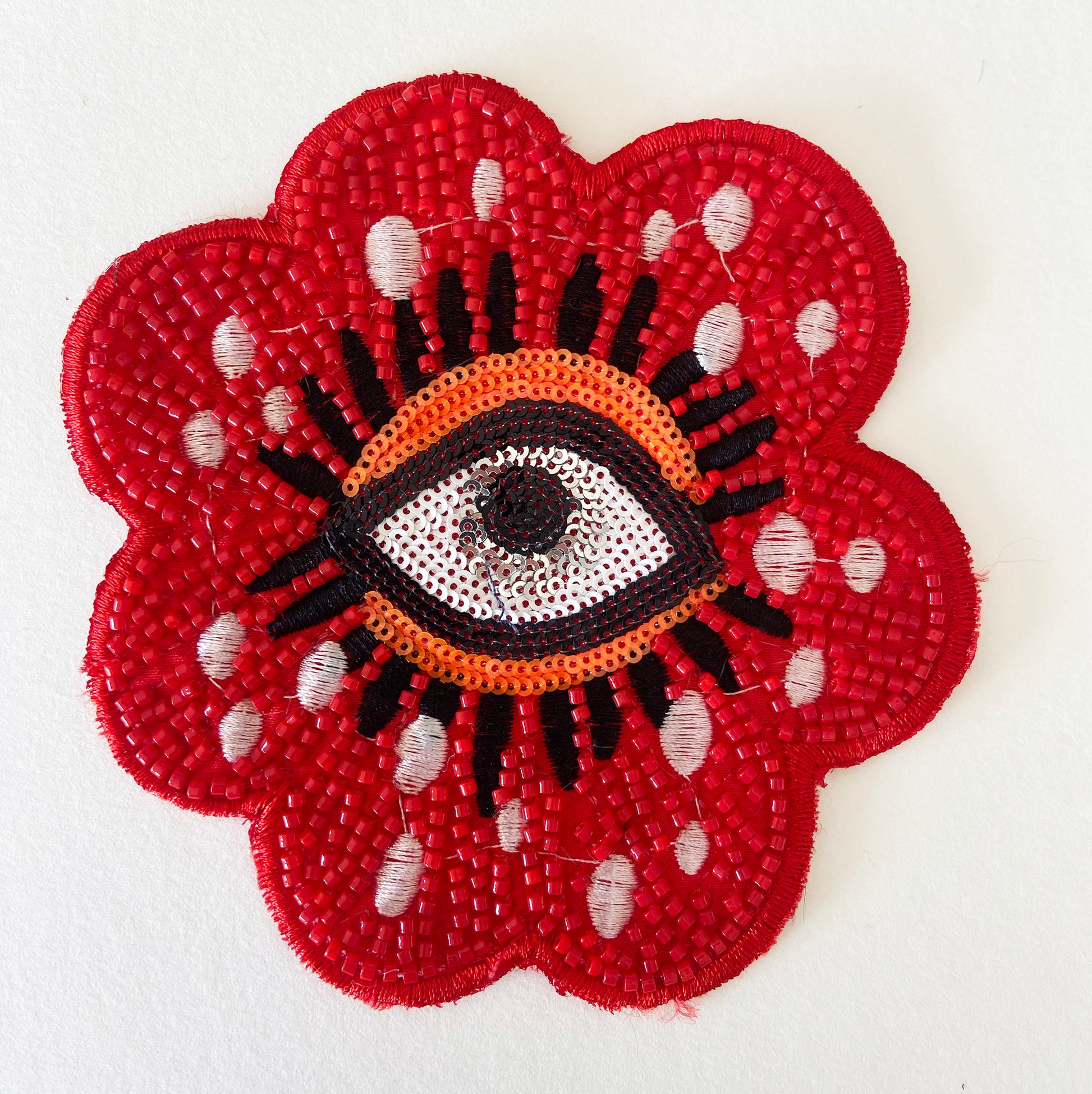 Decorative patch with a red flower design and central eye symbol on a white background