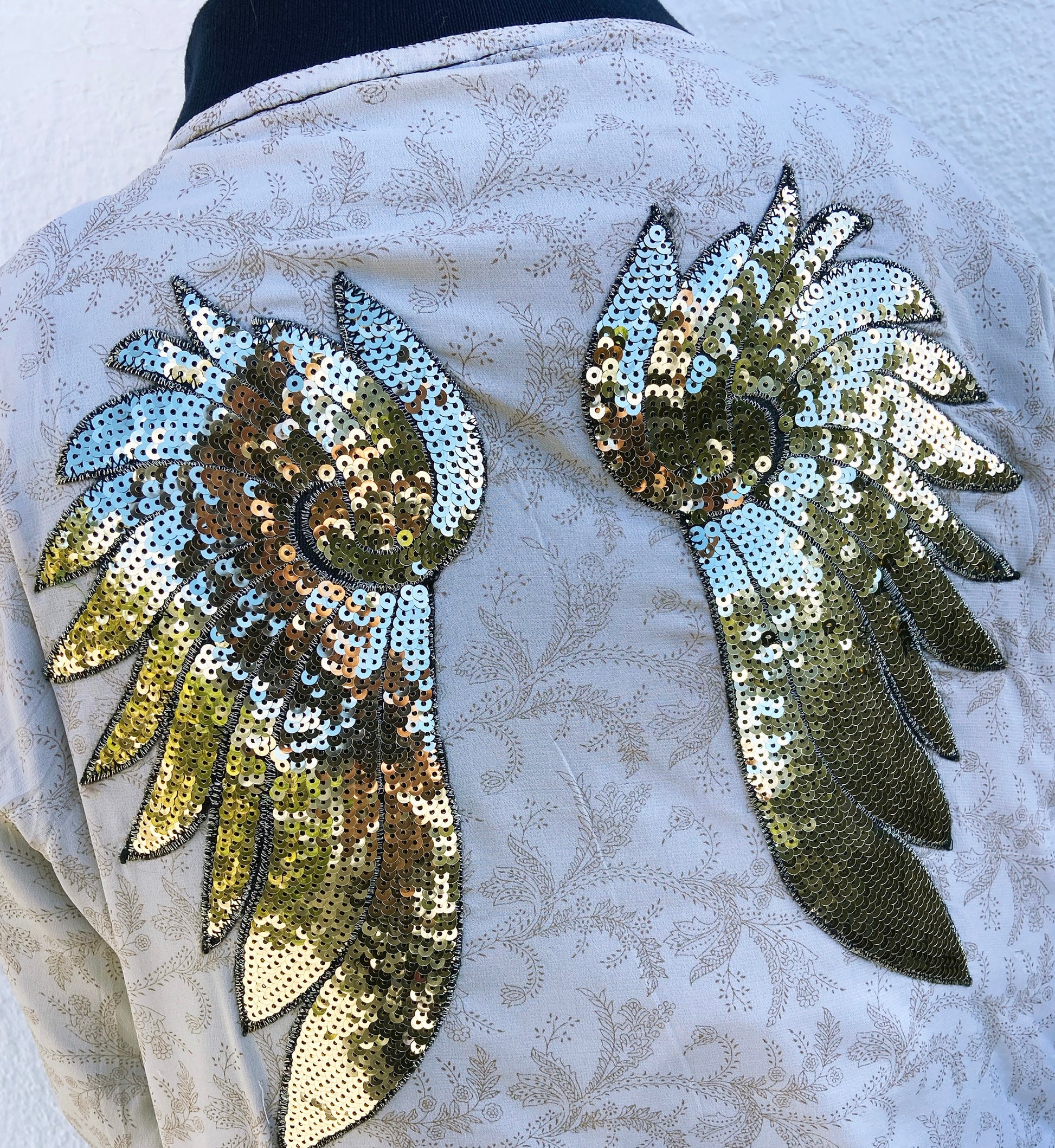 Sequin wing patches sewn onto a cream floral fabric jacket back.